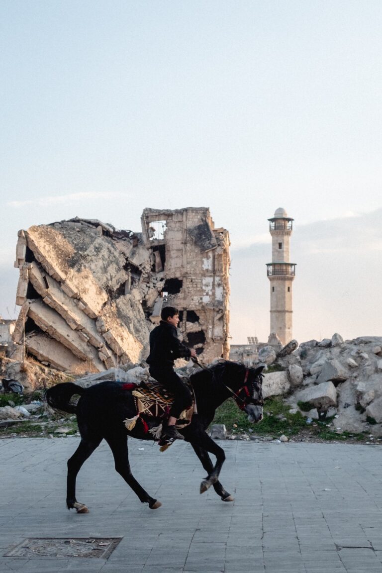young boy riding a horse and in the background the destroyed building of Aleppo