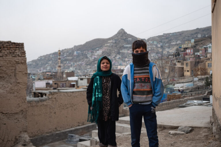 Two Afghan children standing in the cold on a hill overlooking Kabul city.