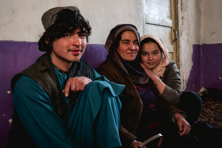Smiling Afghan women and her two children sitting together in a cozy indoor setting in Bamyan, Afghanistan.