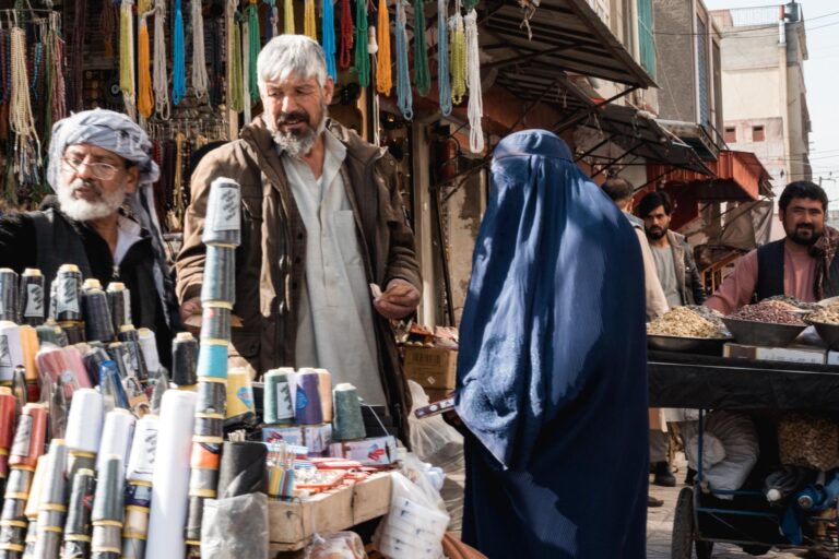 Vibrant market scene with Afghan men and a woman wearing a burka buying and selling fresh produce in Mazar-i-Sharif, Afghanistan.