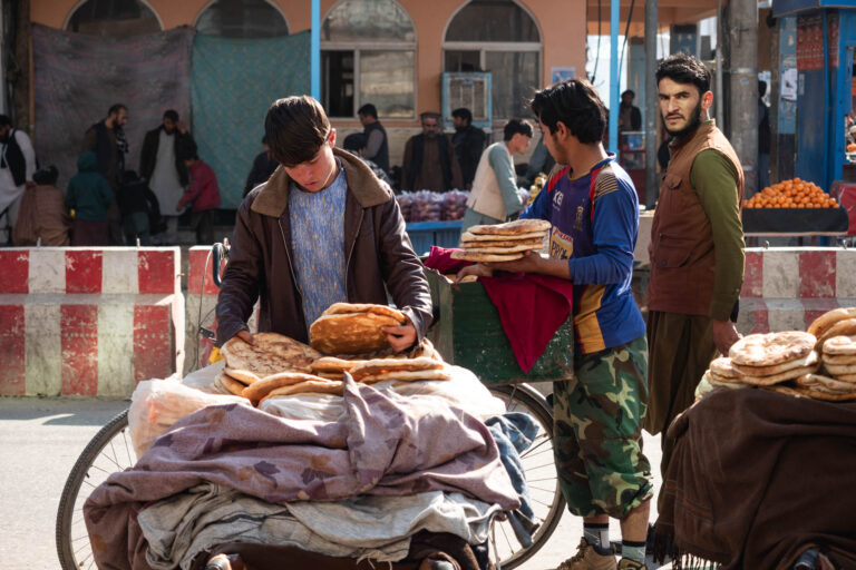 Afghan man selling bread at an open market, surrounded by colorful produce in Kunduz, Afghanistan.