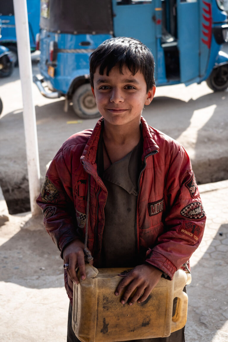 Smiling Afghan boy holding a yellow jerrycan in a street market in Kunduz, Afghanistan
