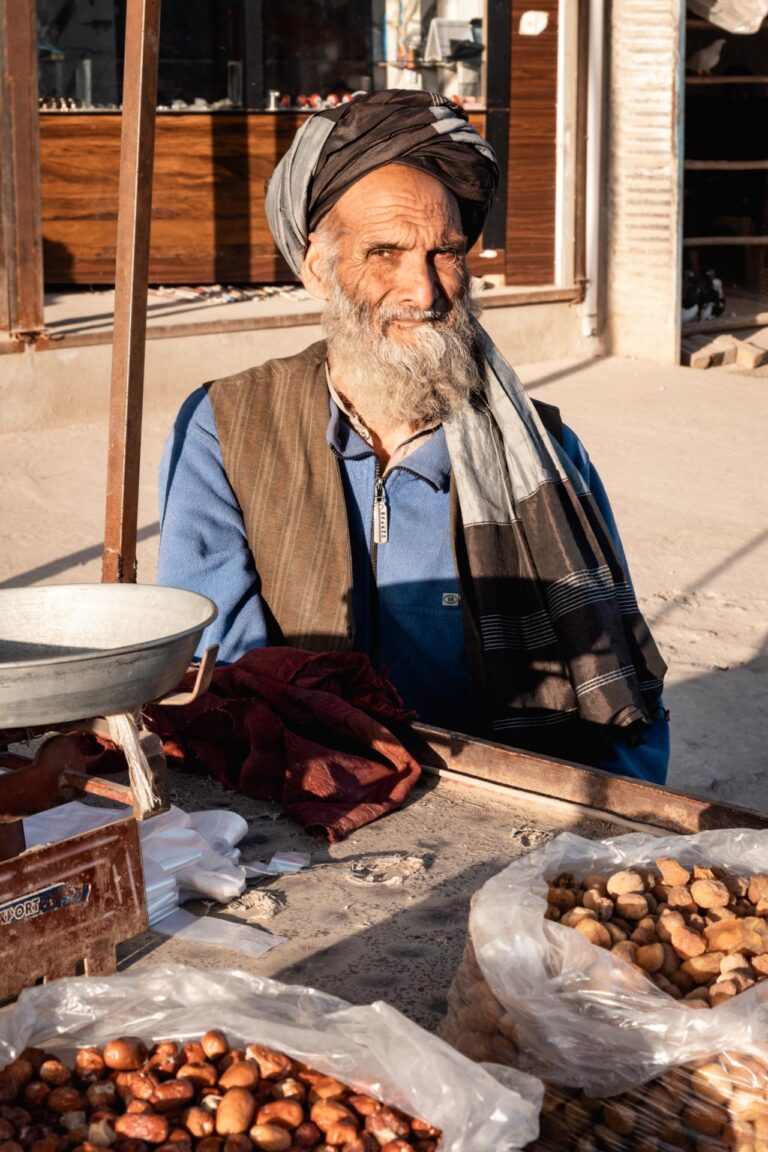 An elderly Afghan man seated behind a table, selling fresh nuts at a local market in Kunduz, Afghanistan