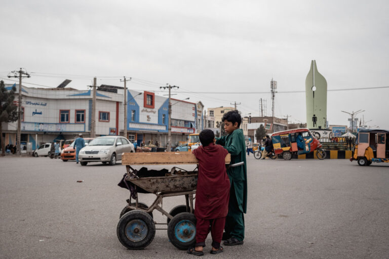 Bustling street scene with two young men pushing a cart near colorful buildings in Herat, Afghanistan.