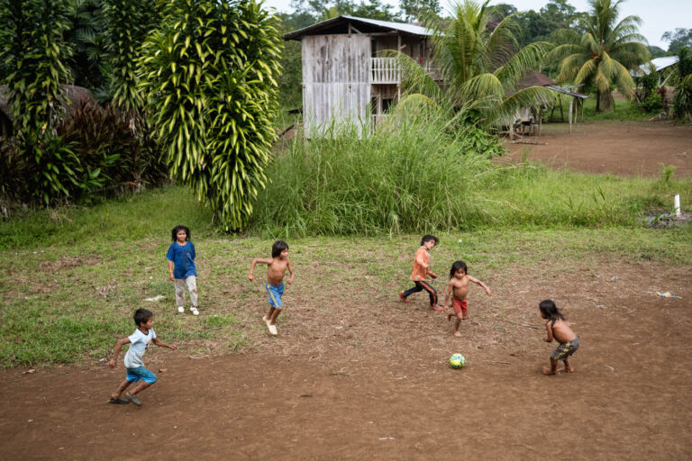 Achuar kids playing football barefoot on muddy village ground in Ecuador’s Amazon