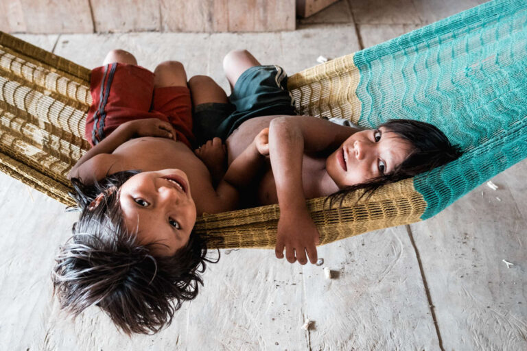 Achuar children resting in a hammock inside a traditional wooden house, Ecuadorian Amazon