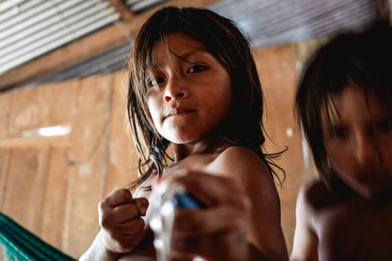 Achuar woman and children indoors, warm light illuminating traditional Amazonian life