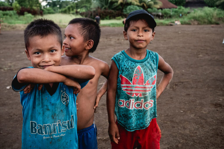 Group of Achuar boys smiling and hugging each other in their jungle village.