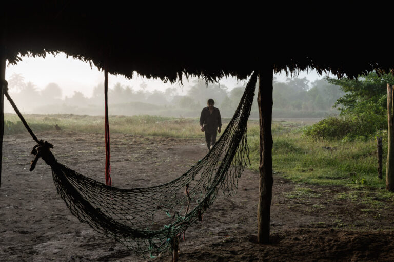 Traditional Achuar hammock shelter at dawn, fog hanging over the Amazon forest.