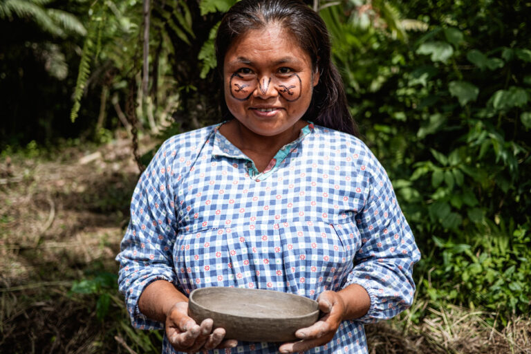 Smiling Achuar woman holding cocoa pods, standing in front of jungle crops
