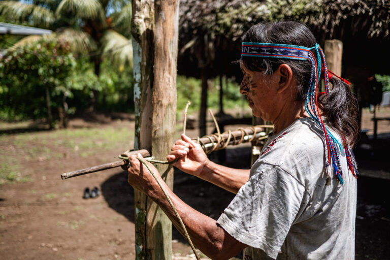 Achuar man carving wood outside a house, Amazonian craftsmanship in progress
