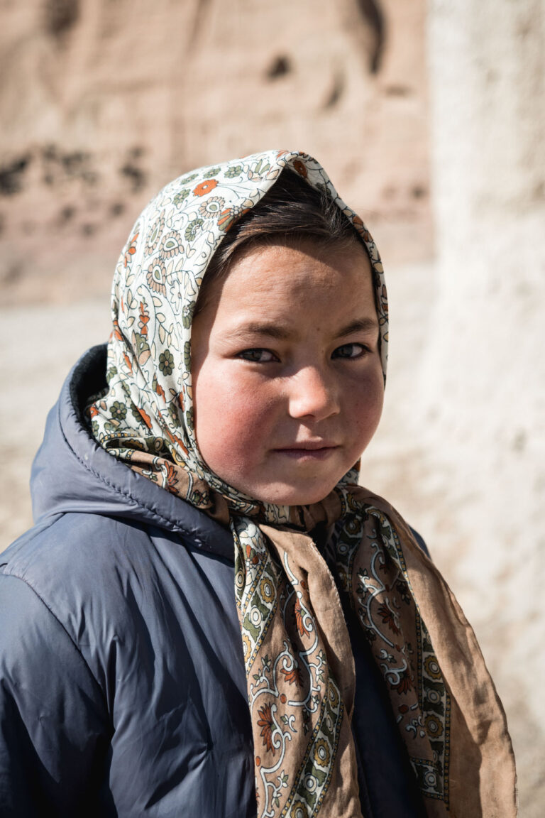 Portrait of a young Afghan girl in a traditional woolen shawl, staring deeply into the camera.