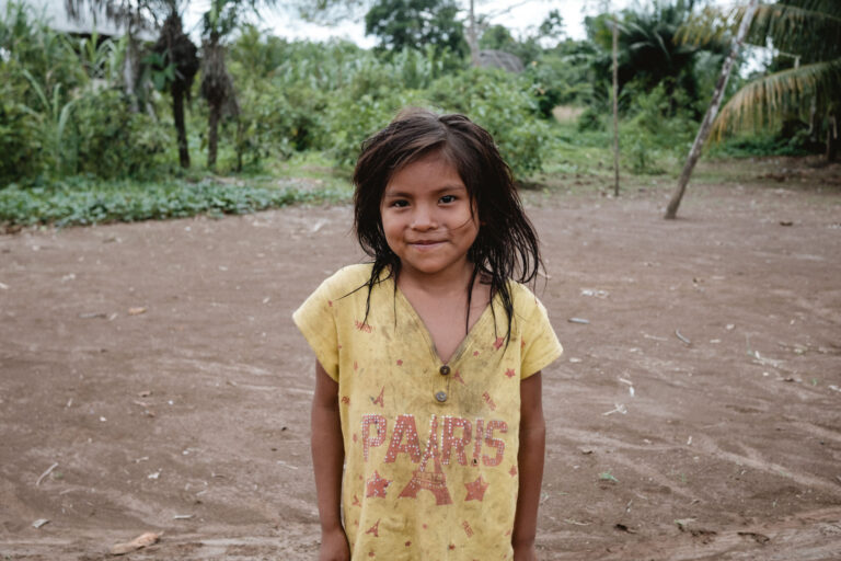 Achuar girl in a colorful skirt smiling shyly under the bright Amazonian sunlight.