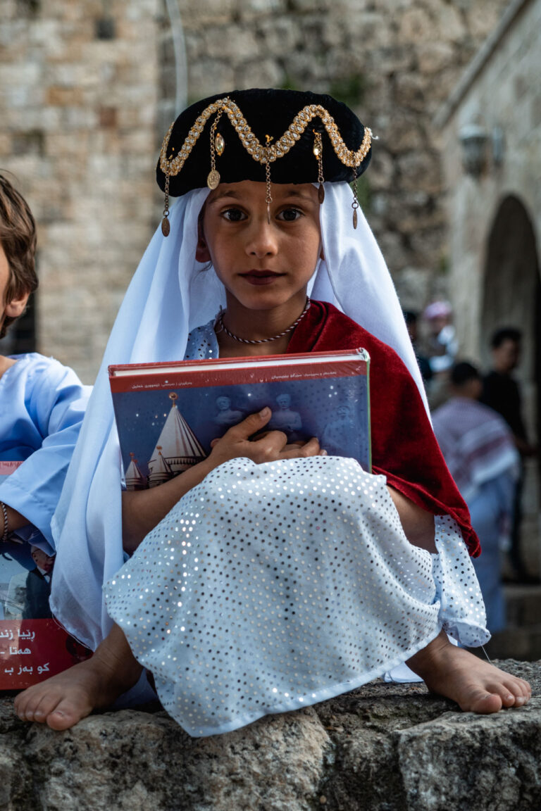 Kurdish girl in ceremonial clothing, sitting outside the temple of Lalish with a pensive look.