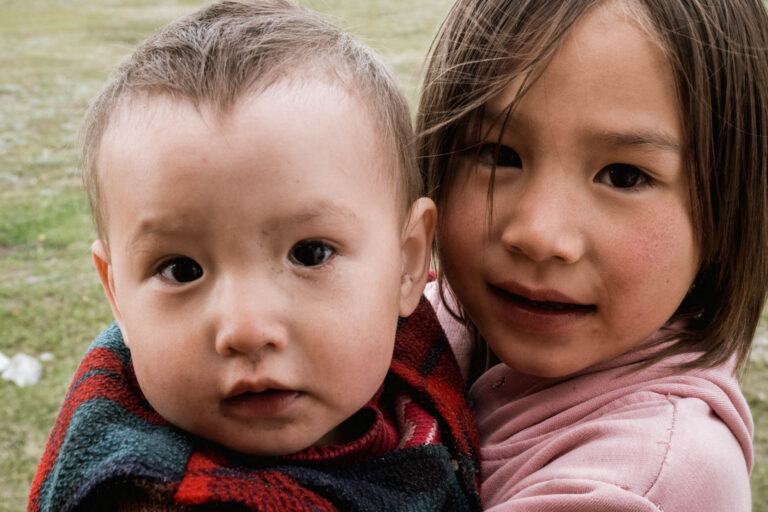 Close-up of two Kyrgyz children, one hugging the other, smiling warmly at Tulpar Lake.