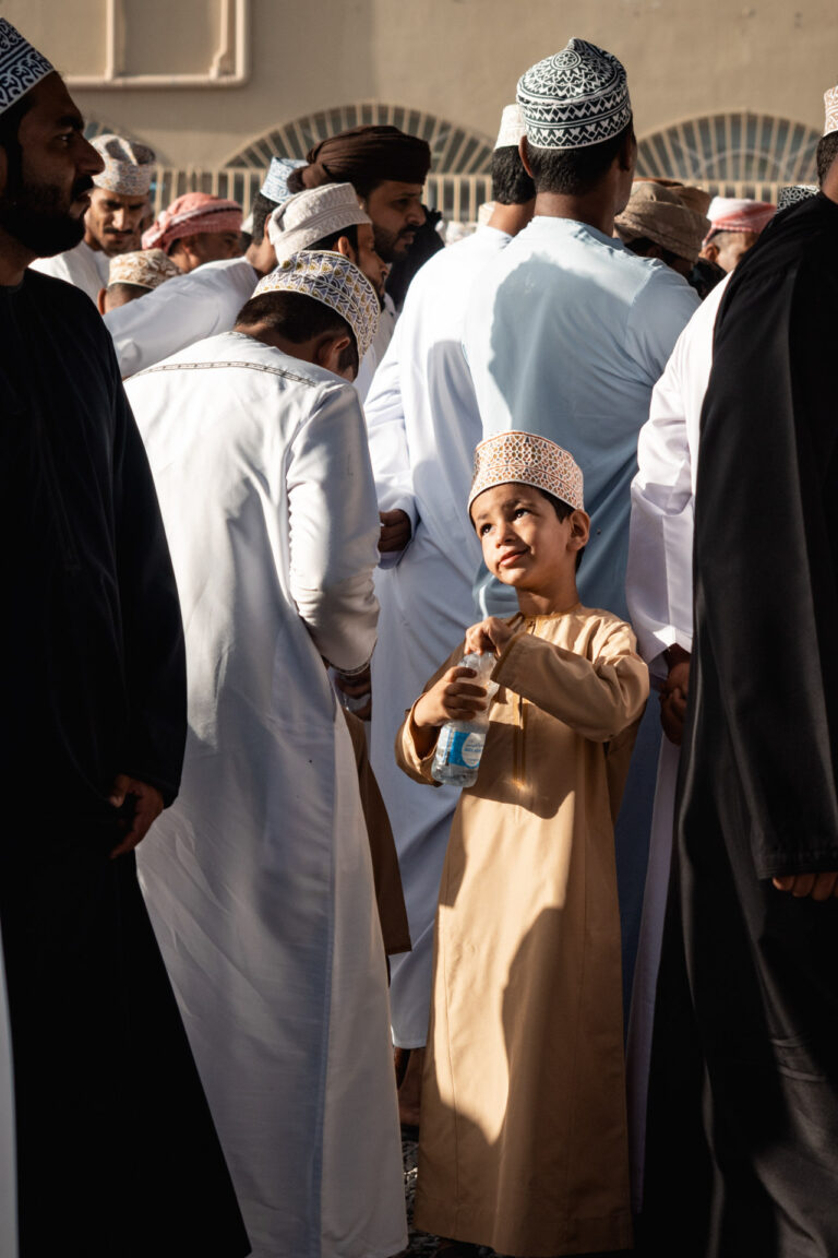 Omani men in traditional dishdashas gathered around goats for sale at Nizwa’s bustling market.