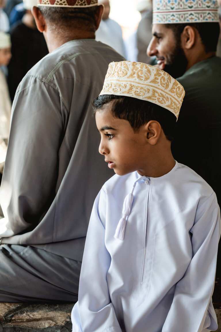 Omani boys dressed in white robes watching the busy Friday livestock market in Nizwa.