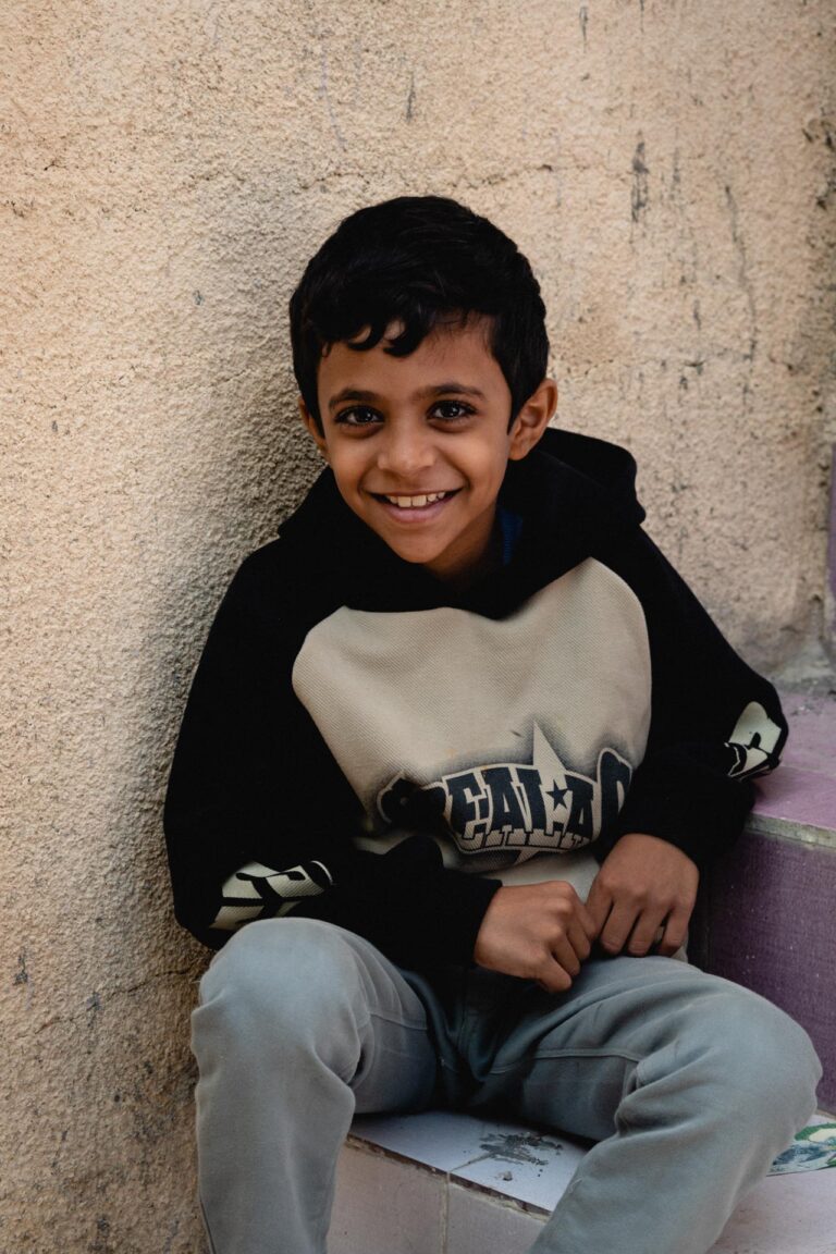 Smiling young Omani boy in traditional attire, seated in the mountainous region of Jabal Hatt.