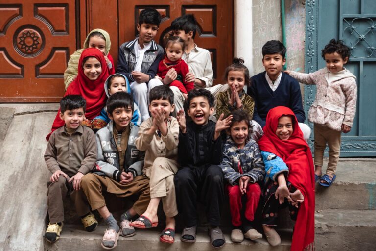 Group of children and adults posing joyfully in a crowded alleyway in Peshawar.