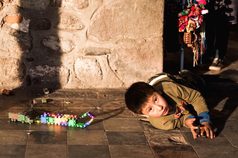 Peruvian child lying on a cobbled street, gazing into the camera with a playful smile.