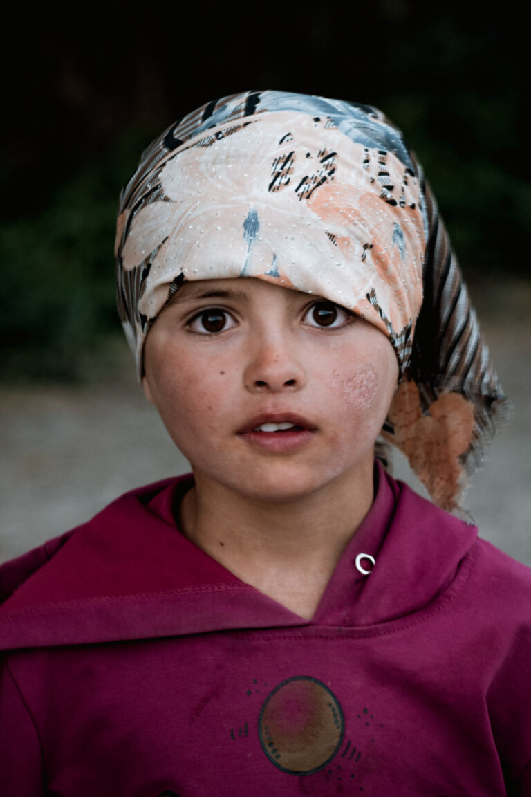 Young Tajik girl with rosy cheeks and a floral headscarf, gazing seriously into the lens.