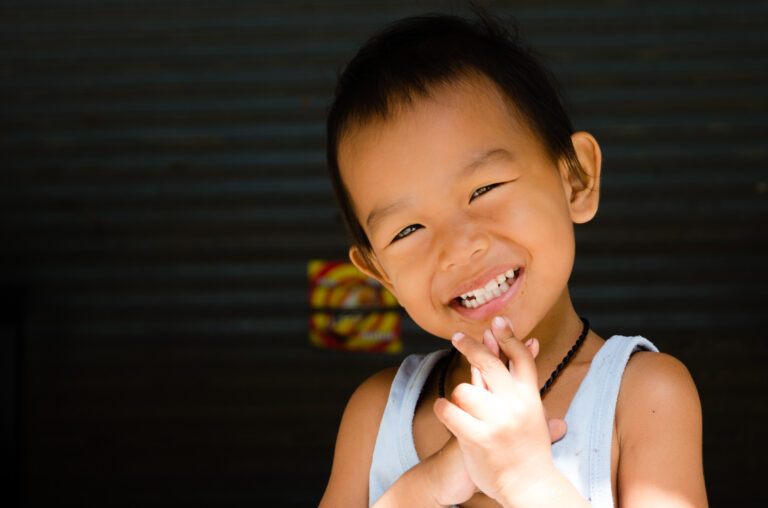 Young Thai child smiling joyfully with hands clasped in a playful pose