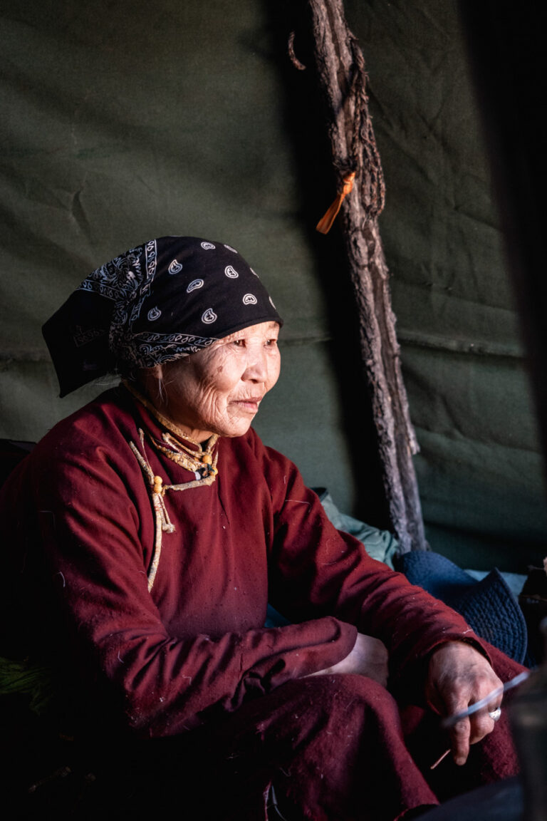 Young Tsaatan woman smiling inside the family tent, bathed in firelight.