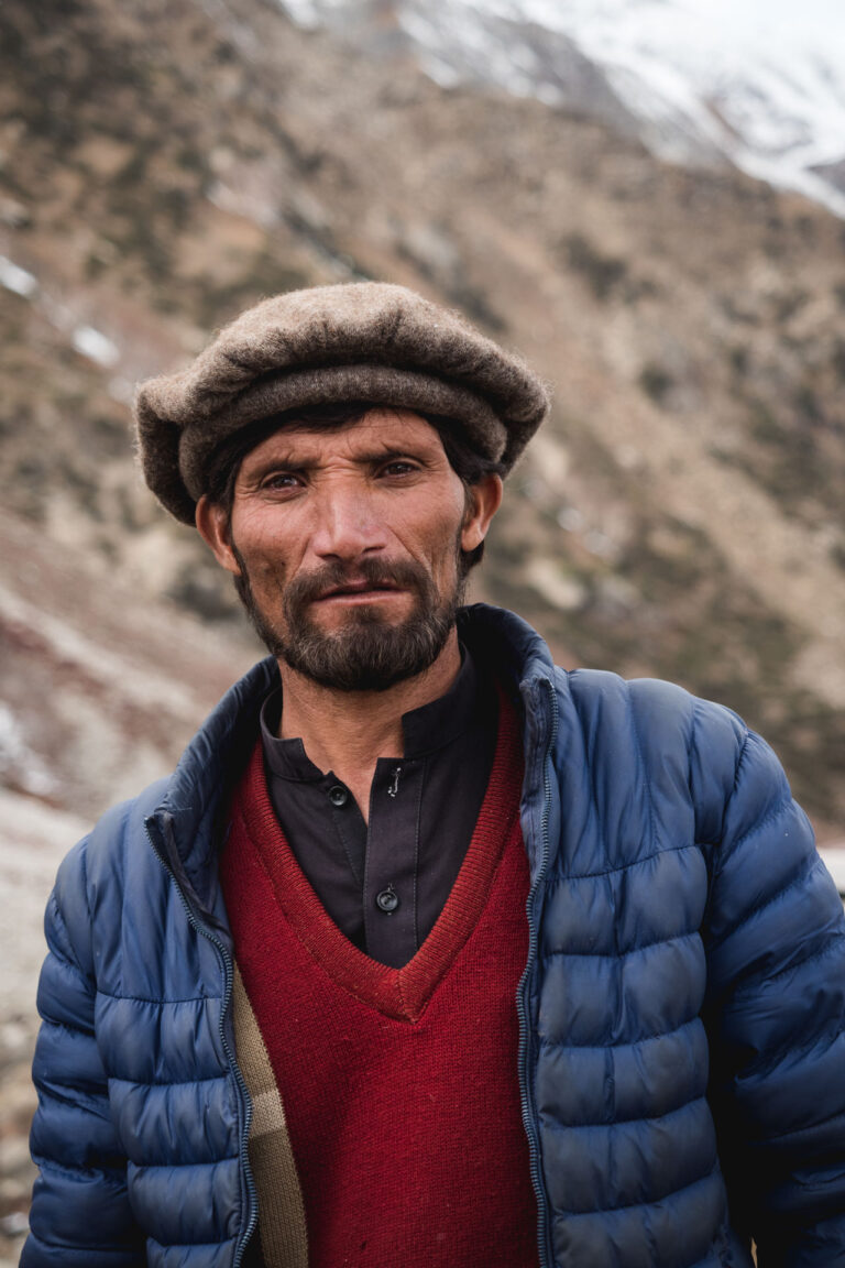 Smiling man with a beanie standing in front of a mountainous landscape in Fairy Meadows, Pakistan.