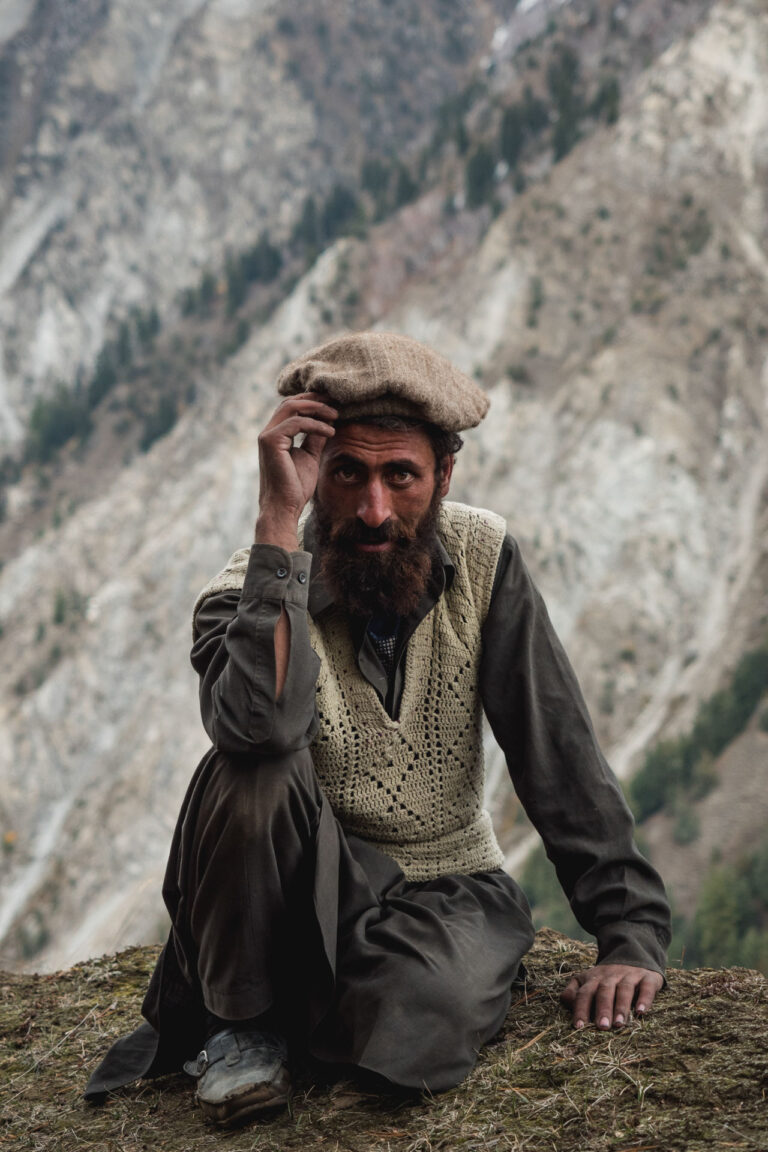 Man sitting on a grassy slope surrounded by pine trees at Fairy Meadows, Pakistan.
