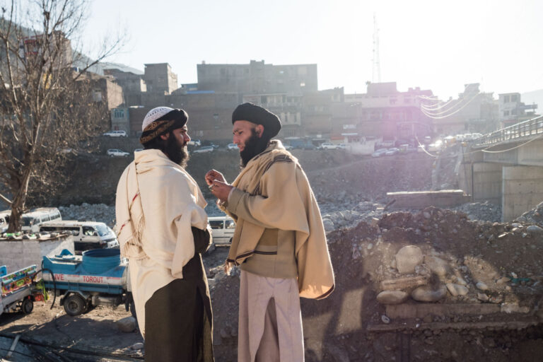 Two Taliban wearing traditional shawls, conversing near a riverside in Madyan, Swat valley, Pakistan.