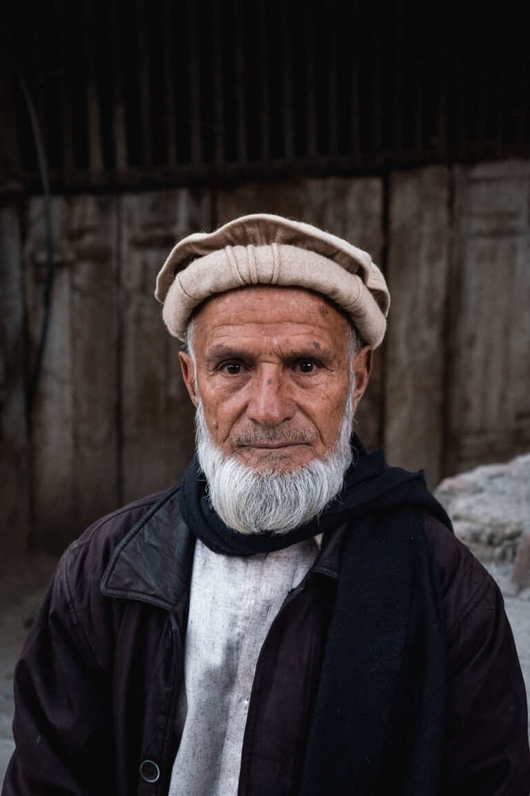 Elderly man wearing a traditional woolen cap and shawl, smiling modestly in Bahrein, Swat valley, Pakistan.