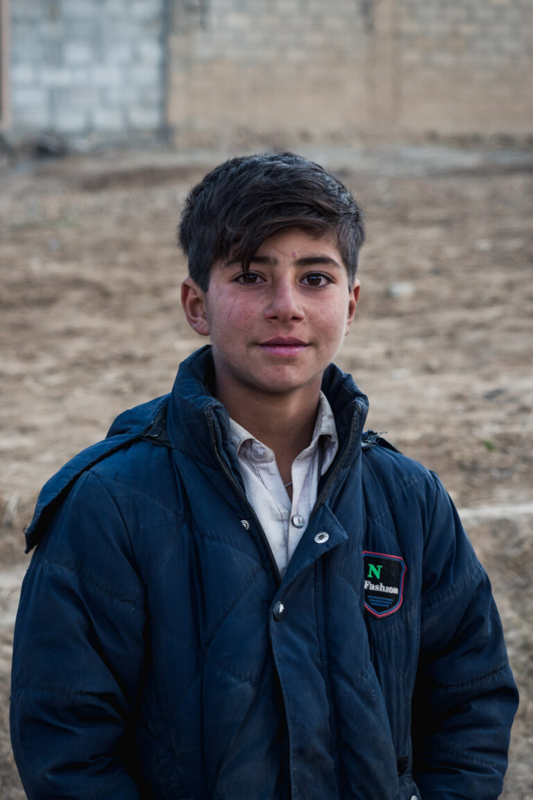 Smiling teenage boy standing in front of a stone wall in Bayün village, Swat valley, Pakistan.