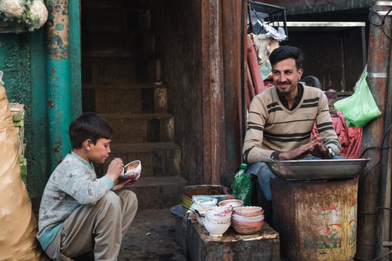 Young boy eating at a shop of a smiling man inside a small blacksmith shop in Madyan, Swat valley, Pakistan.