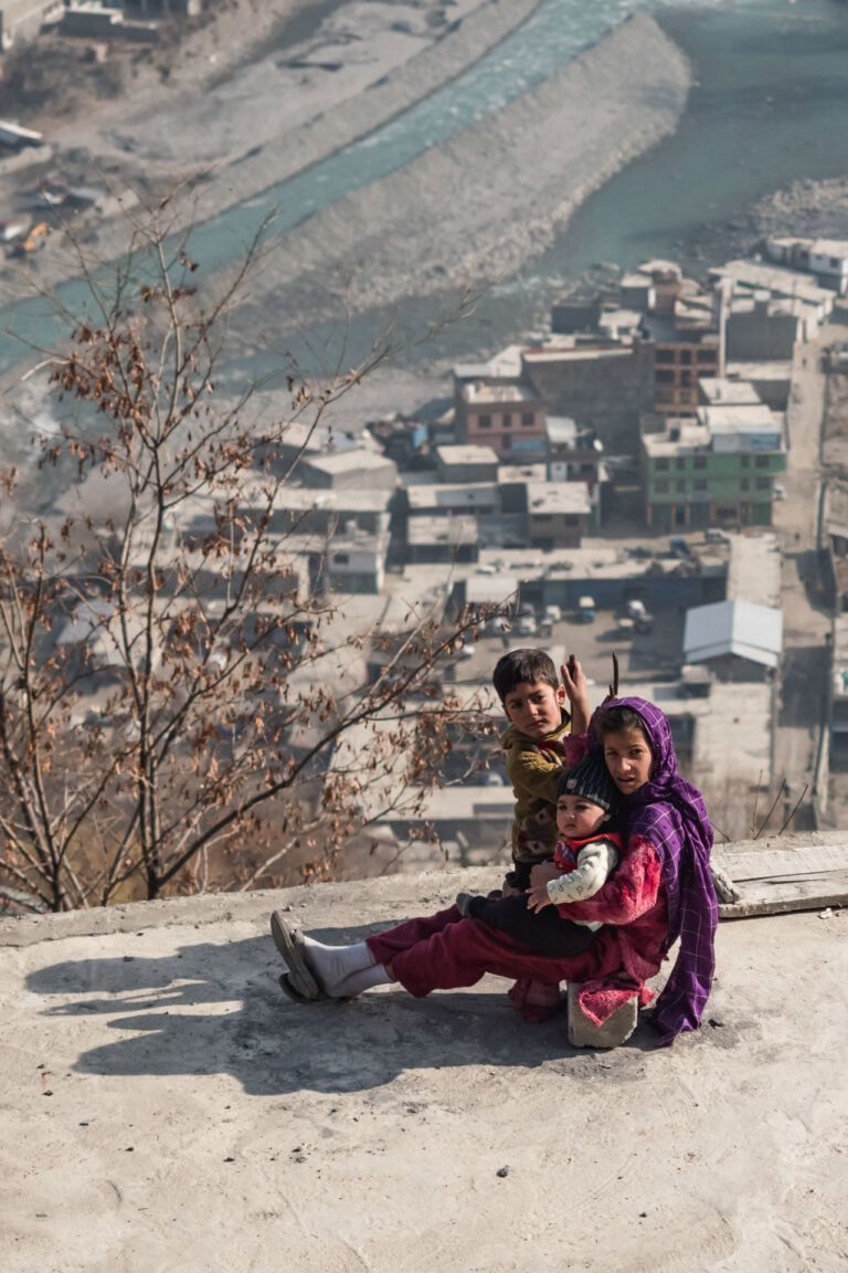 Young girl sitting on a rocky hill, with her two brothers, overlooking the vast Chitral valley in northern Pakistan.