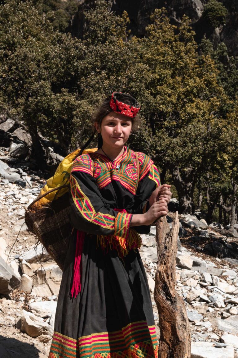 Local Kalasha girl hiking through the rugged trails of Bumburet valley surrounded by rocky peaks.