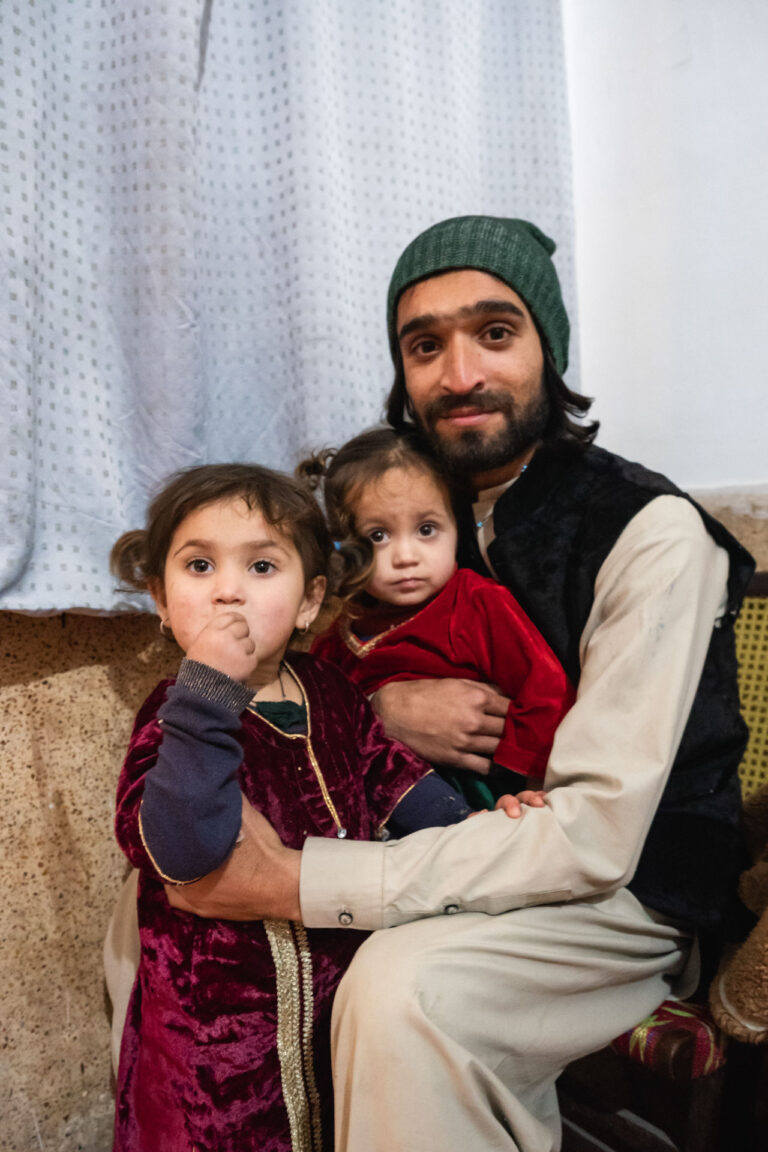 Pashtu Pakistani father sitting with his two children in a warmly lit indoor space in Peshawar, Pakistan.