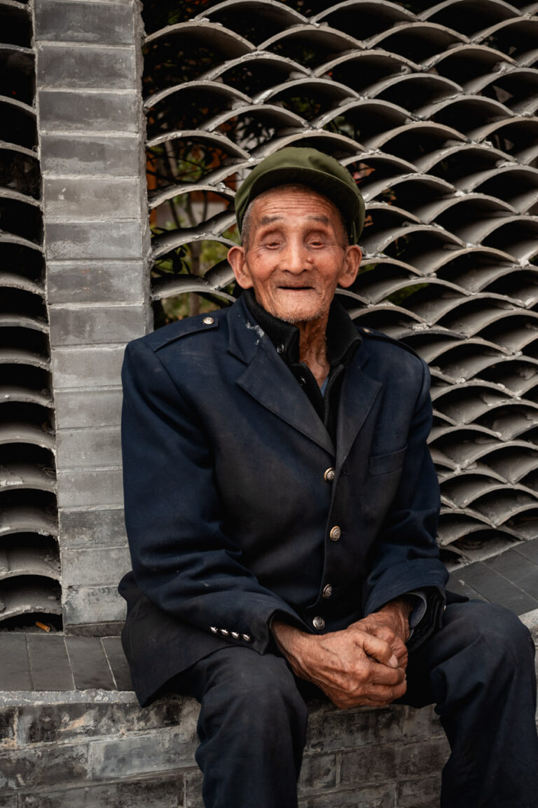 Beautiful elderly Tibetan man with a characteristic face, sitting in the town of Moxi, Tibet.