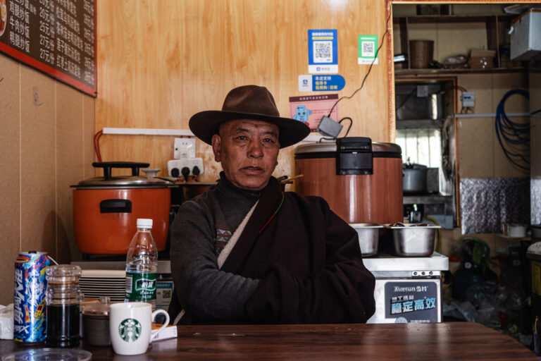 Tibetan man in traditional clothing and hat, waiting for his food in a restaurant in Tagong.