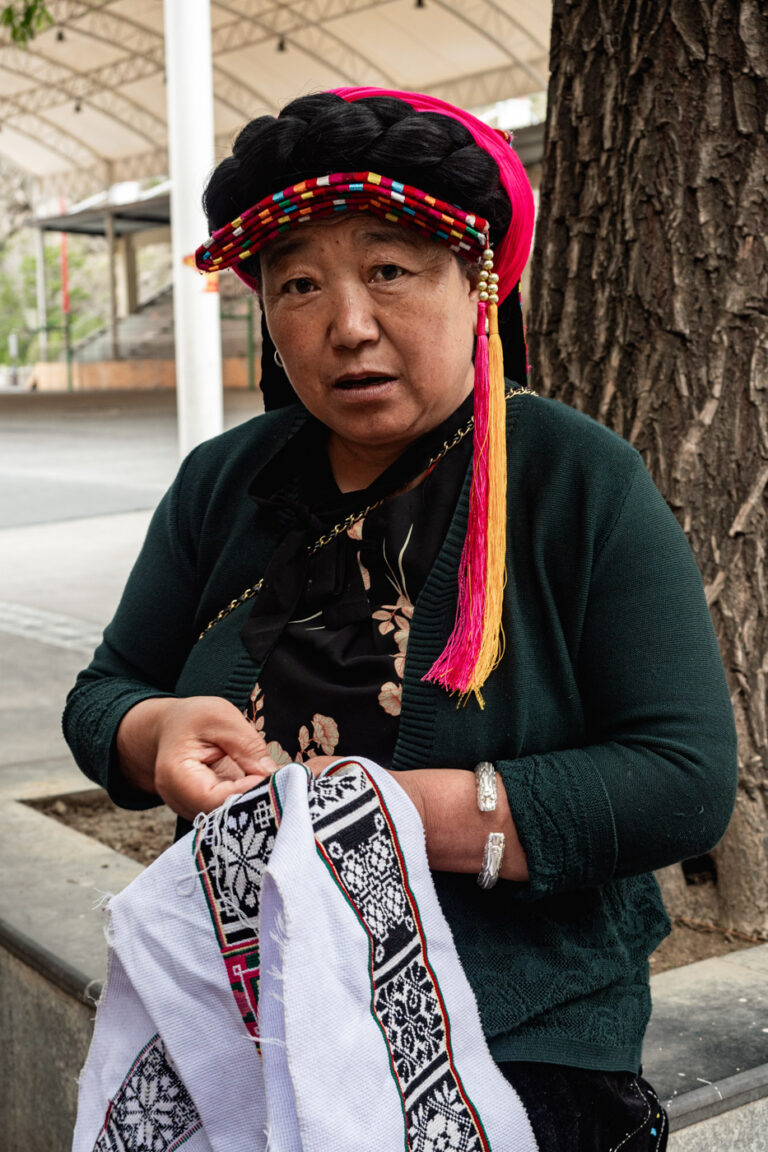 Gyarong woman in traditional colorful clothing, embroidering in the village of Danba.