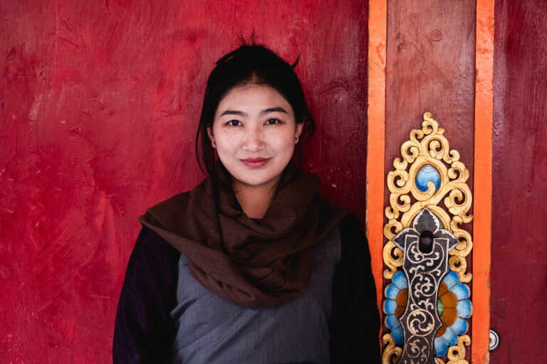Young Tibetan Khampa woman in black coat posing against red wall