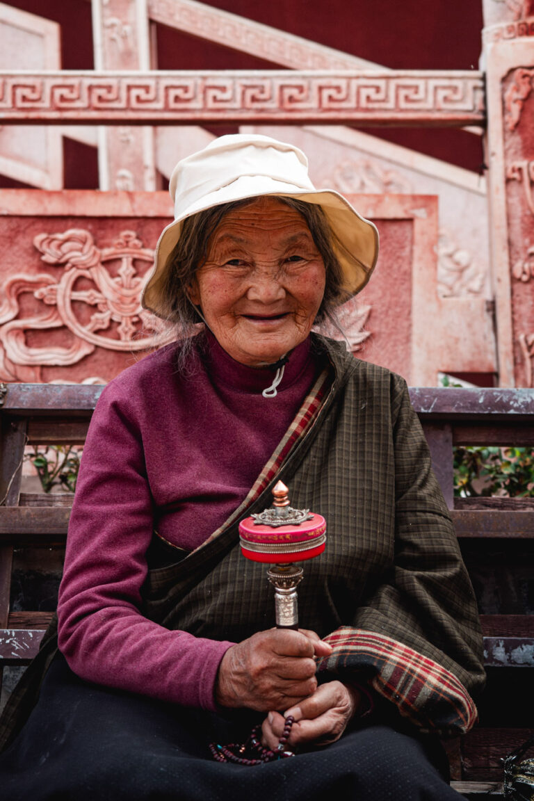Smiling Tibetan khampa woman seated with prayer wheel, China Tibet