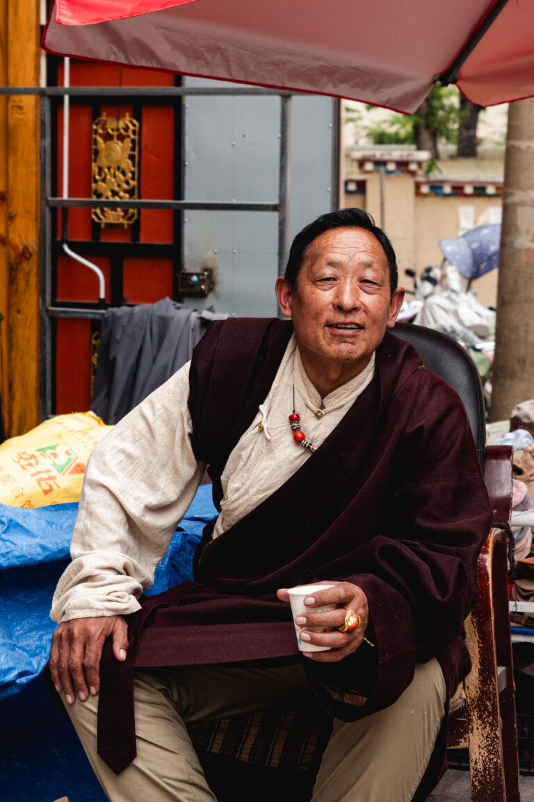 Seated Tibetan man in orange jacket and boots, China.
