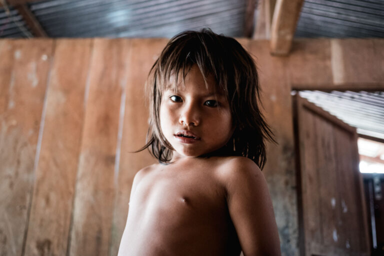 Indigenous Achuar boy inside this wodden house, looking directly into the camera in the Amazon rainforest.