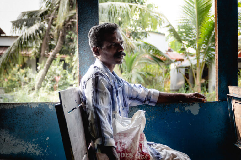 Indian man standing in a boat in Kerala with palmtrees and green nature