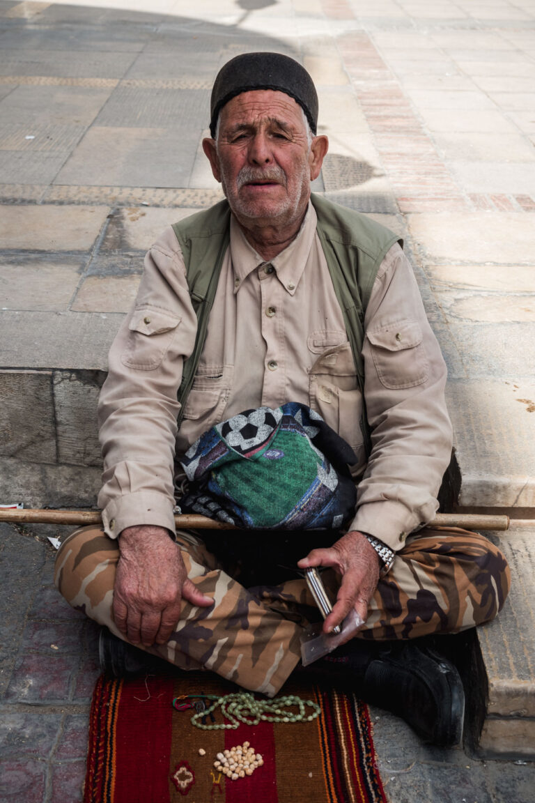 Elderly man sitting cross-legged with a handwoven carpet inside Vakil Bazaar, Shiraz.