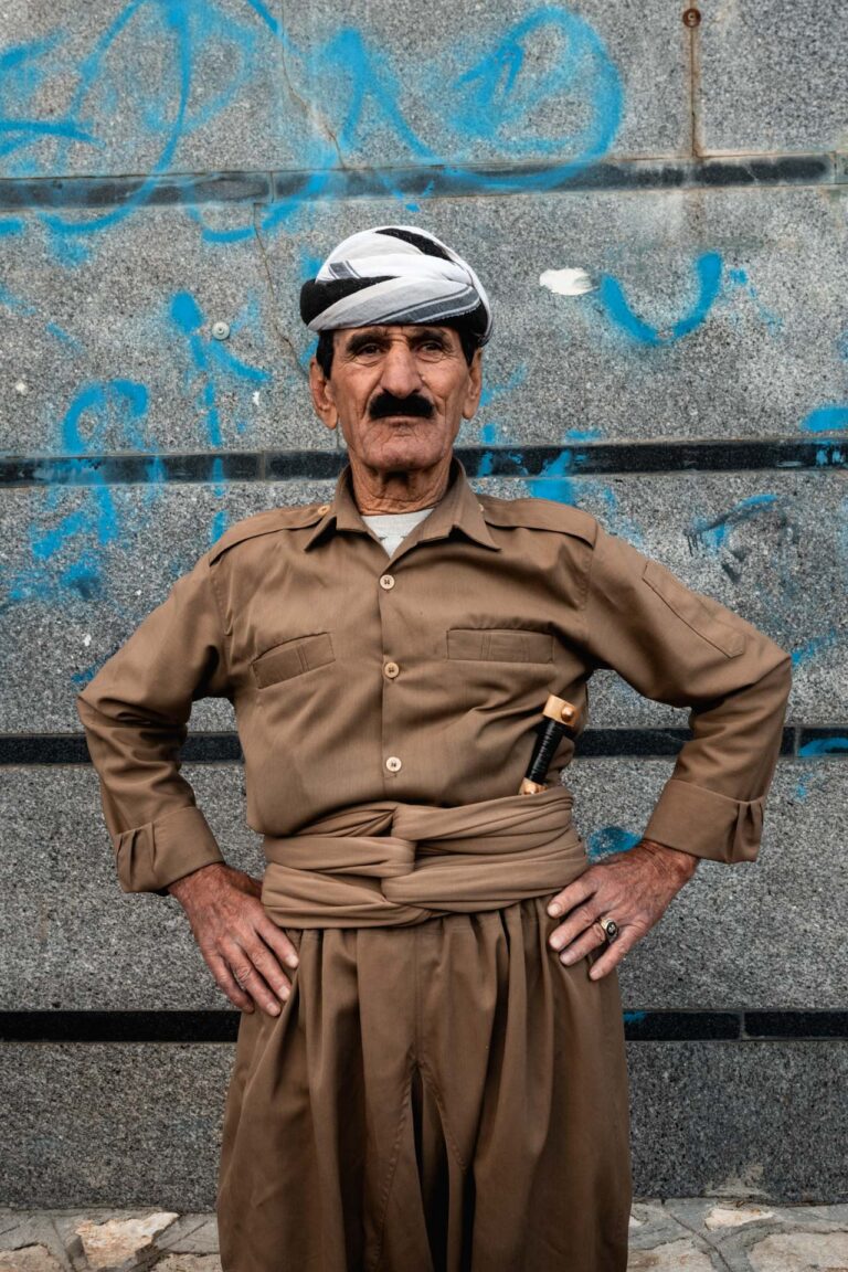 Kurdish man in traditional attire, standing confidently against a graffiti-covered wall in Iran.