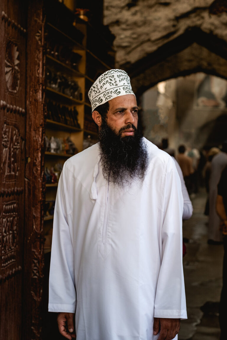 Omani man with a long beard and white turban standing amidst the bustling crowd at Nizwa Market