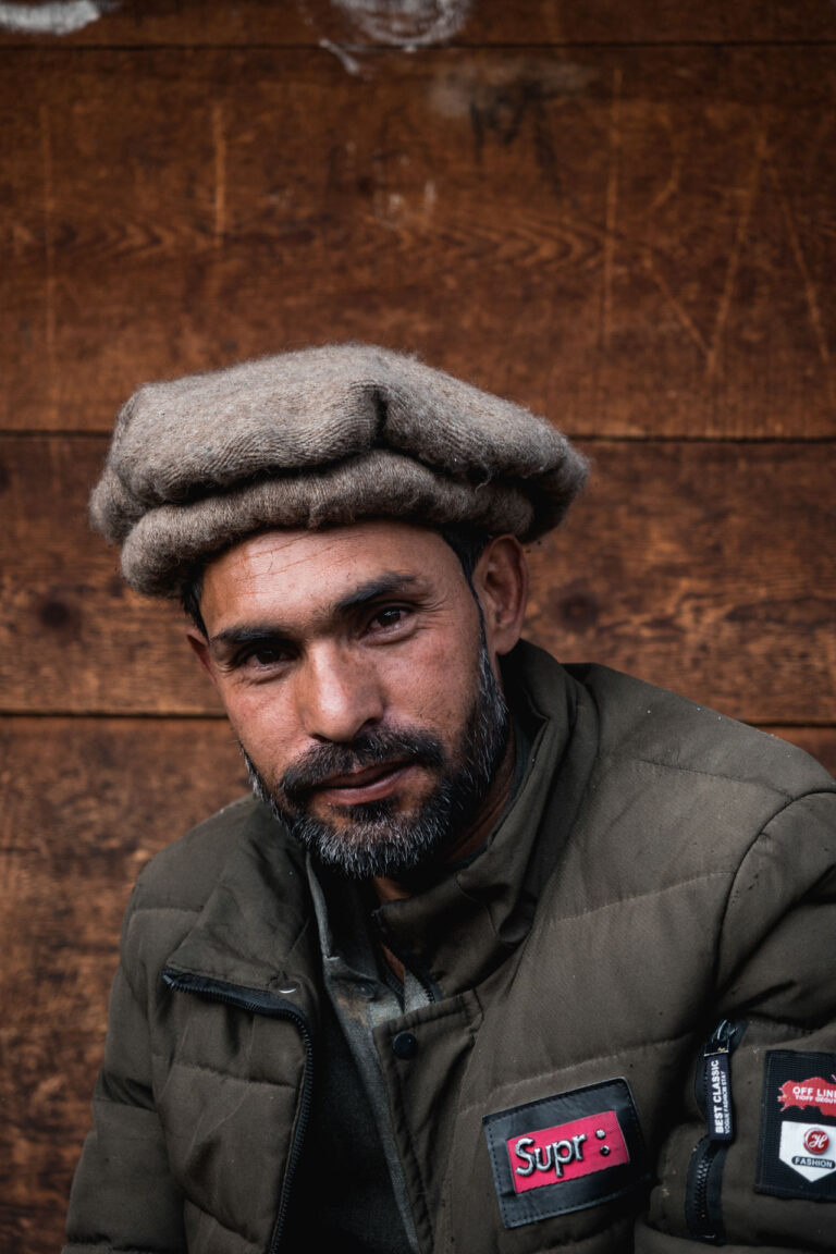 Bearded man wearing a hat sitting in a wooden interior with a warm smile at Fairy Meadows.
