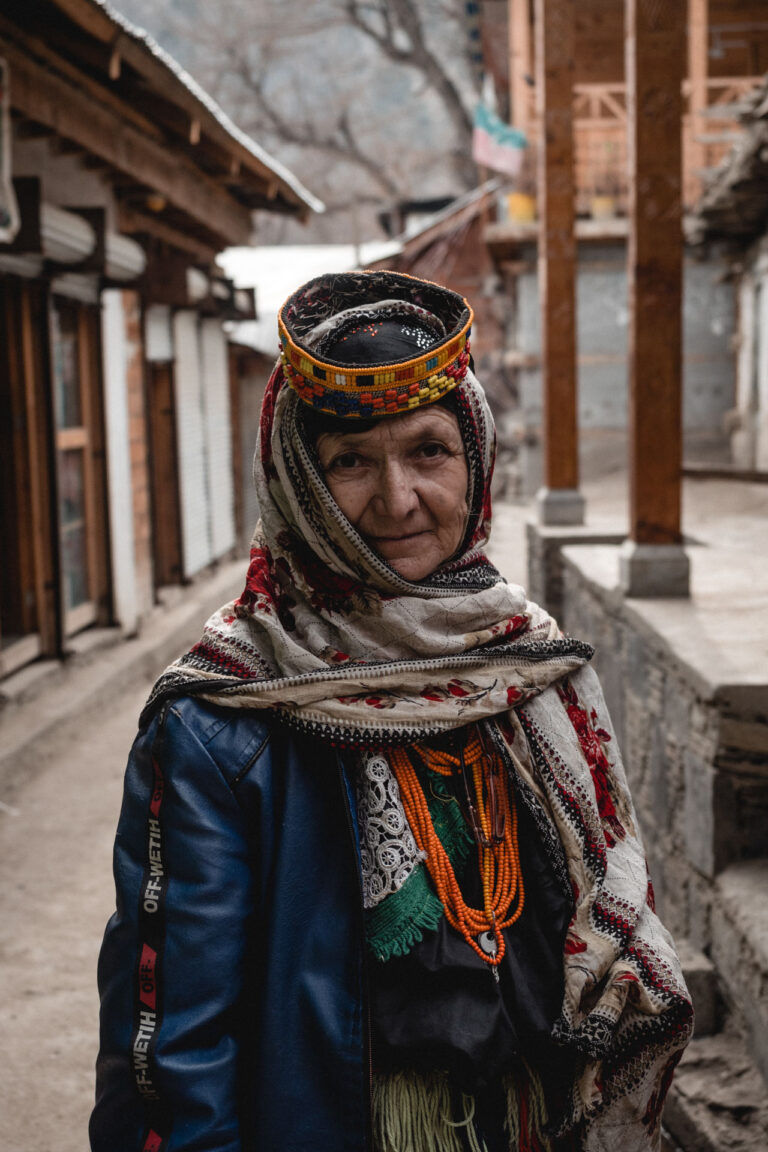 Elderly Kalasha woman standing outdoors wearing vibrant Kalasha attire in Bumburet Valley.