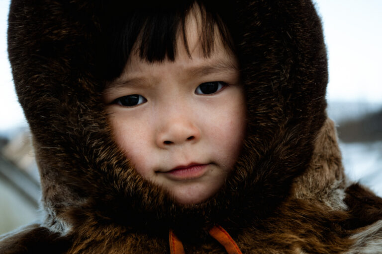 Close-up portrait of Nenets girl in reindeer fur, Siberian tundra, Russia.